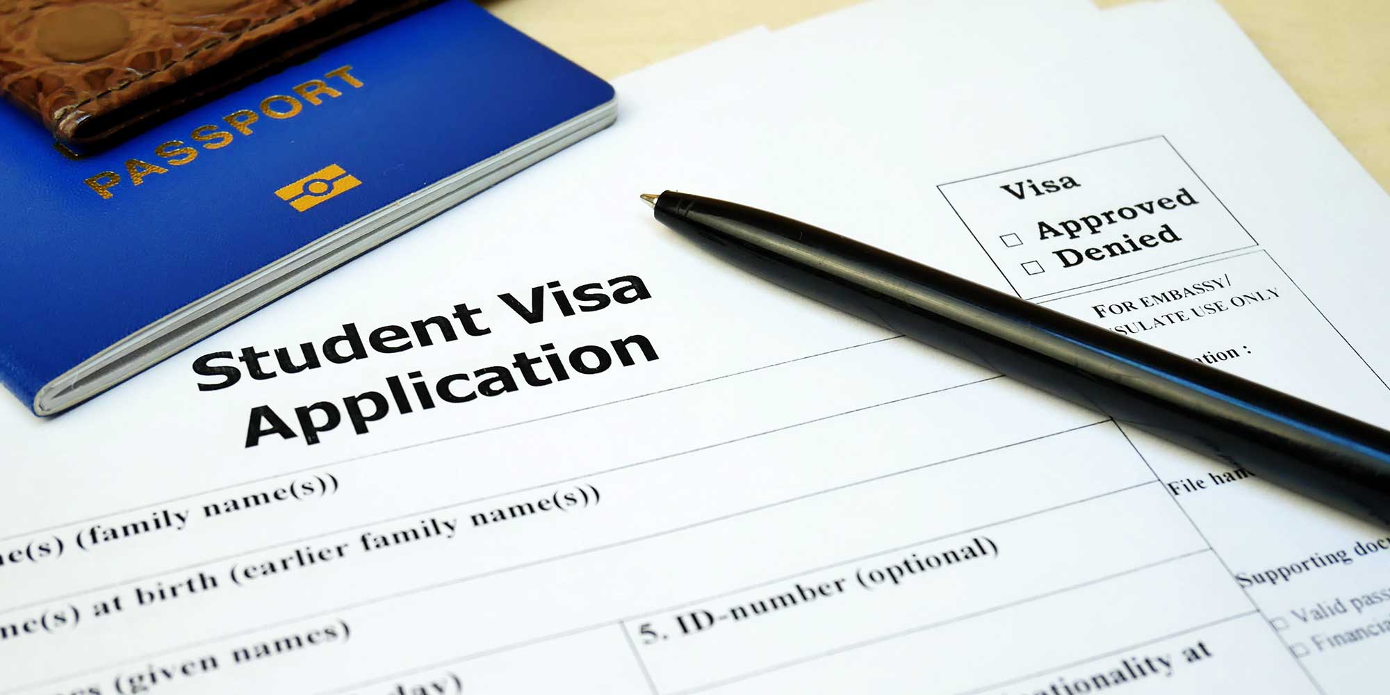 Pen and passport atop a sheet of paper that says Student Visa Application